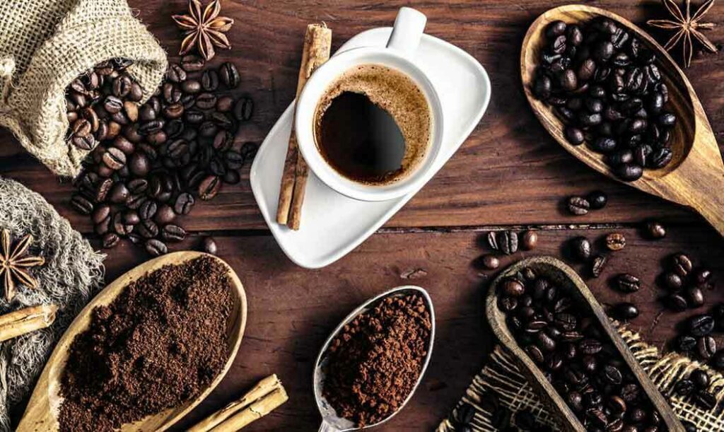 A cup of coffee surrounded by ground and whole coffee beans.