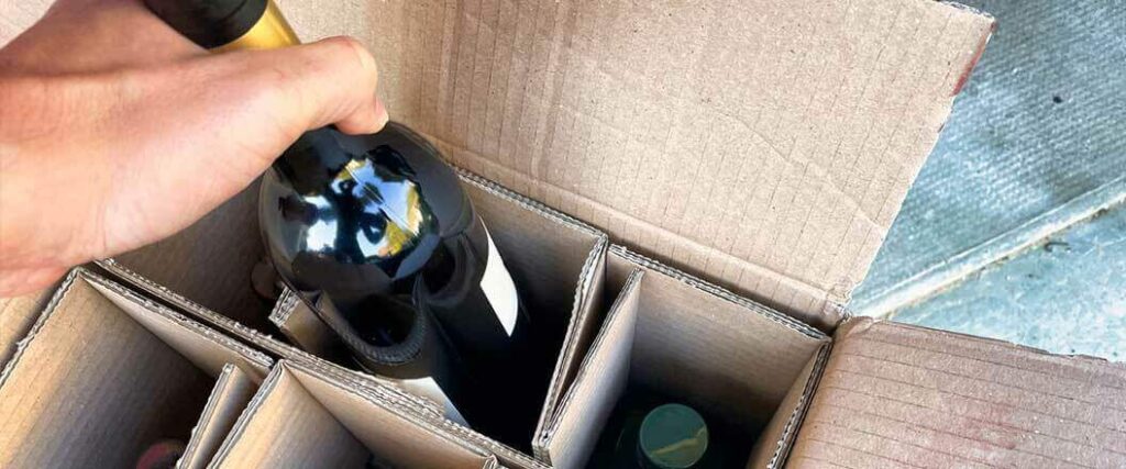 An individual removing a single bottle of wine from a case.