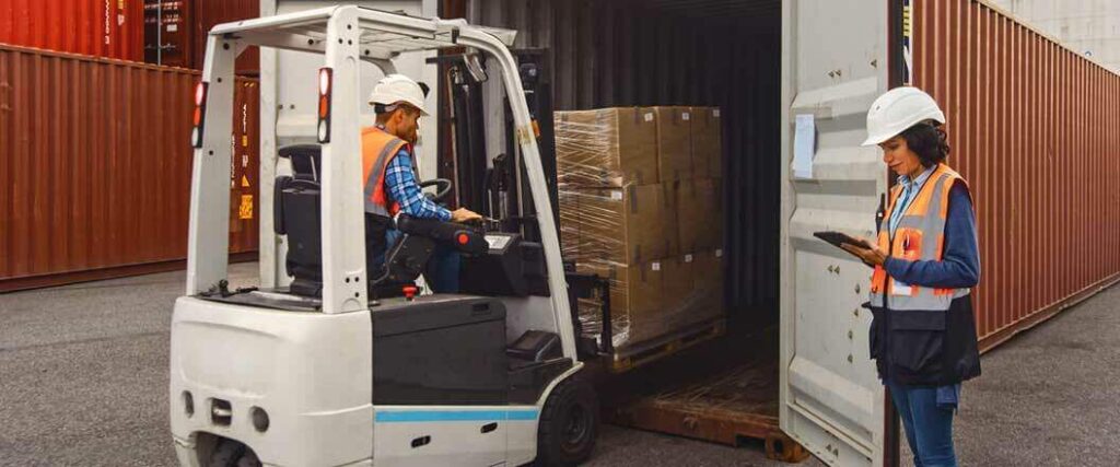 A port worker loading a pallet of freight into a container