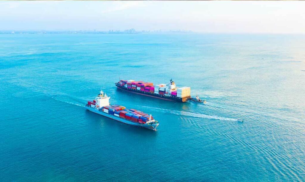 A pair of loaded cargo ships at sea being guided by an escort vessel.
