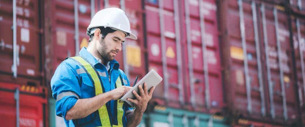 A dock worker looking over paperwork next to a stack of cargo containers