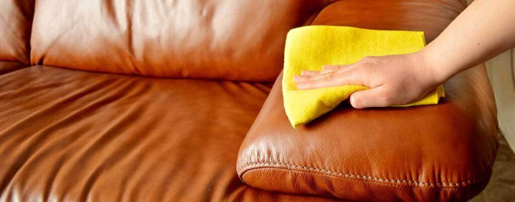 Hand with rag cleaning arm of leather sofa