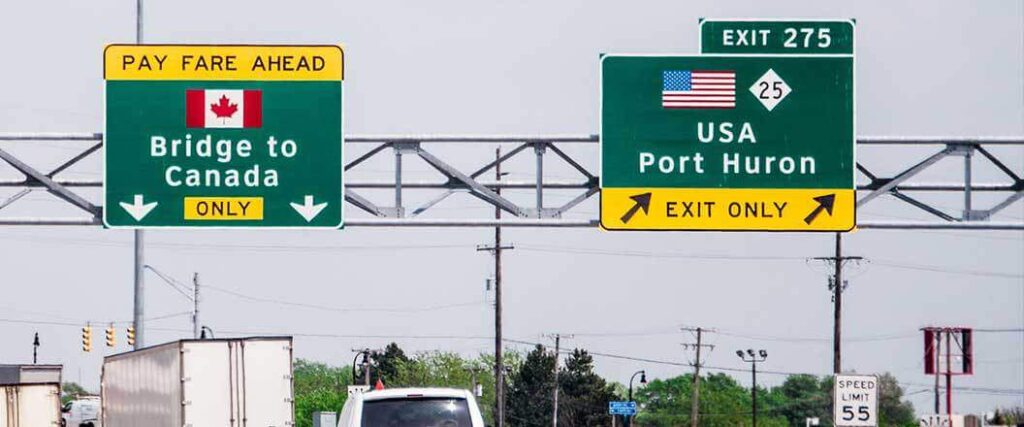 Highway road signs indicating directions to US or Canada near a border crossing. 