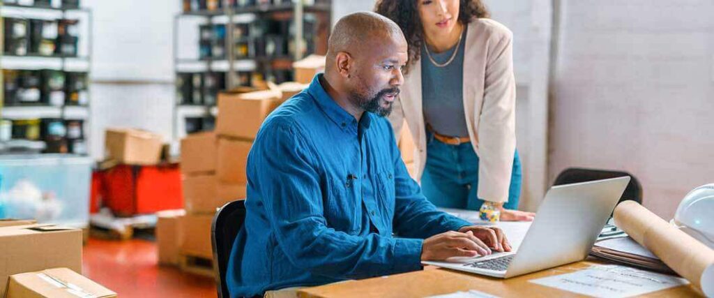 A man operating a laptop computer while a woman watches him over his shoulder.