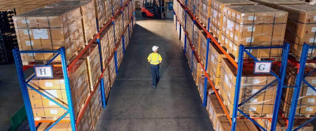 An interior view of a warehouse with a worker walking between two aisles.