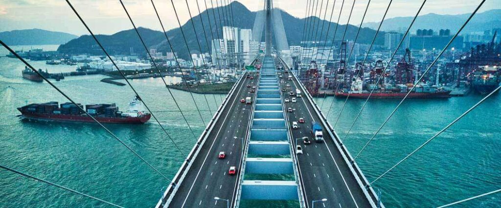 Cargo ships cruising underneath a suspension bridge.
