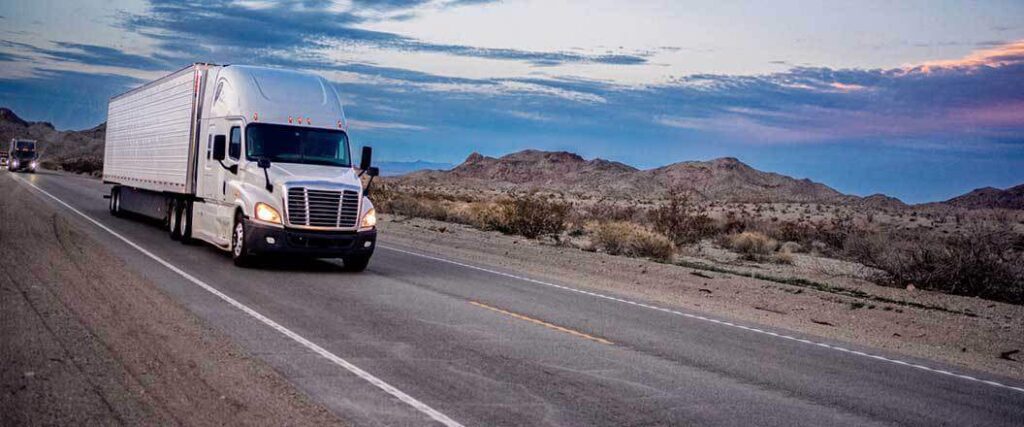 Two semi trucks with enclosed trailers traveling on a desert highway.
