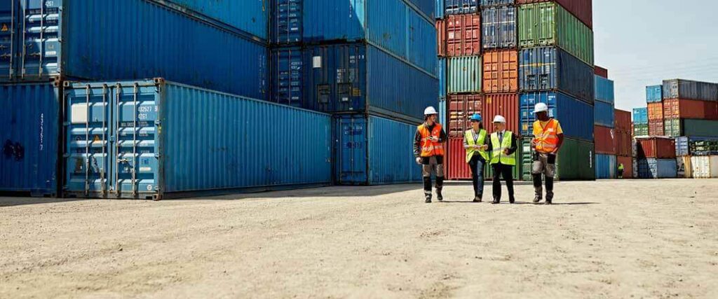 Four dockworkers in the foreground with stacks of cargo containers in the background.