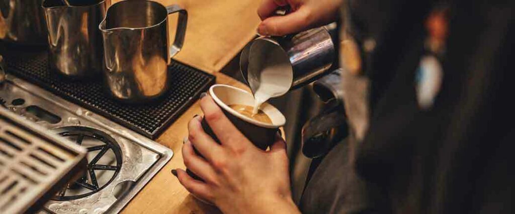 Barista pours cream into a coffee cup. 