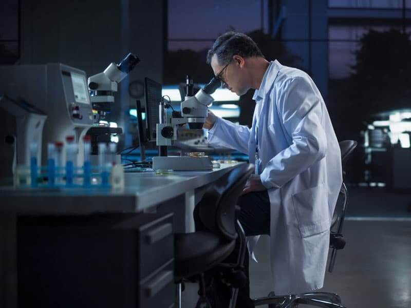 A scientist in a laboratory examining a specimen with a microscope.