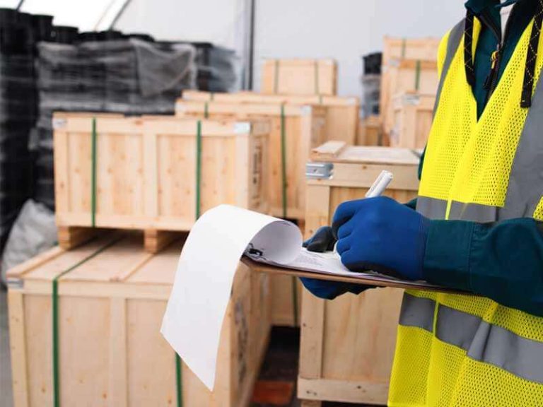 A warehouse worker checking information on a clipboard while standing next to several wooden shipping crates.