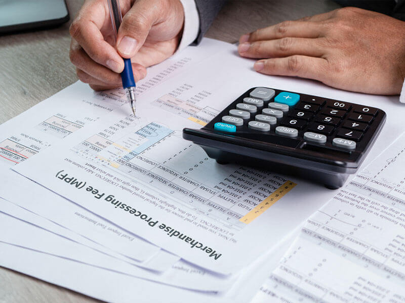 An image depicting a broker seated at a desk, reviewing documents and calculations using a calculator, reinforcing the article's topic: merchandise processing fees